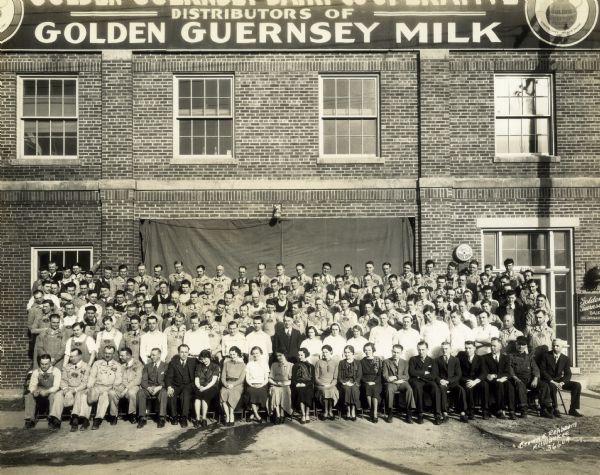 An outdoor group portrait of the employees of the Golden Guernsey Dairy, posed in front of the building.