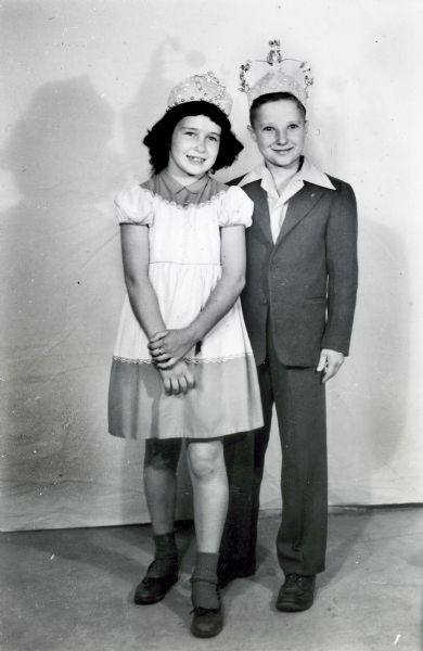 A young boy and girl posed dressed up and wearing a crowns.