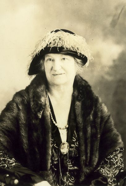 Studio portrait of Helen F Thompson, Park Falls, Wisconsin, wearing a fur and a stylish hat with feathers.






