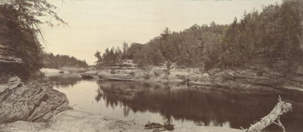 Elevated panoramic view of a section of the Wisconsin Dells and the Wisconsin River visible from the "Sliding Rock." In the lower left hand corner the words "THE WISCONSIN DELLS, FROM SLIDING ROCK. Copyright 1896. by H.H. Bennett." are on a label.