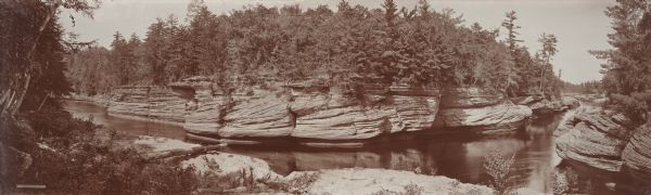 Elevated panoramic view of the narrows of the Wisconsin River in the Wisconsin Dells. On the far left on a label are the words "THE NARROWS, DELLS OF THE WISCONSIN. Copyright 1900. by H.H. Bennett."