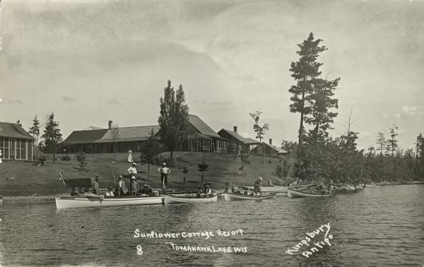 View from lake of the buildings of the Sunflower Cottage Resort. People are canoeing and boating in the lake in front of the resort, and a few people are standing on a pier. Caption reads: "Sunflower Cottage Resort, Tomahawk Lake, Wis."