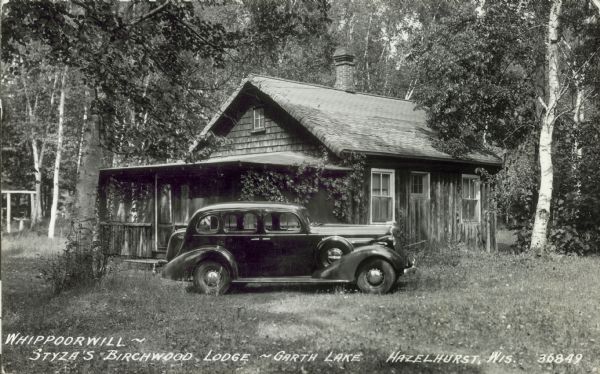 Exterior view of the Whippoorwill cottage at Styza's Birchwood Lodge on Garth Lake. A black automobile is parked in front of the building and trees surround the cottage. Caption reads: "Whippoorwill Cottage ~ Styza's Birchwood Lodge ~ Garth Lake, Hazelhurst, Wis."