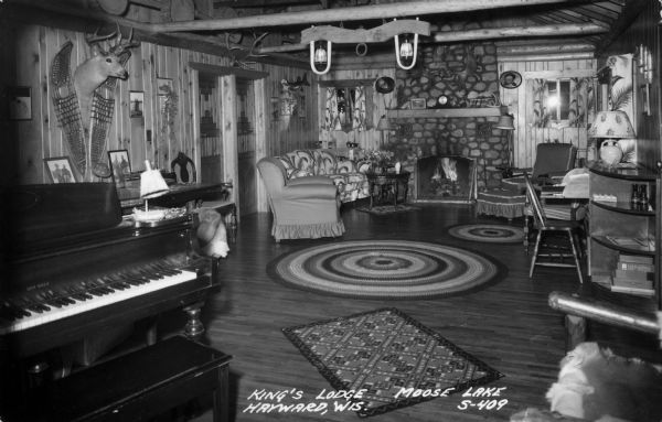 A rustic community room at King's Lodge on Moose Lake. The room contains a piano and fireplace. Caption reads: "Kings Lodge, Moose Lake, Hayward, Wis."