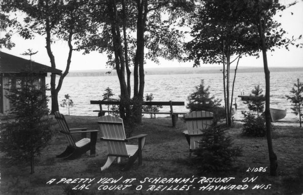 A view of Lac Court O'Reilles at Schramm's Resort, including wood lawn chairs, a bench and trees. Part of a cottage is visible on the left.
