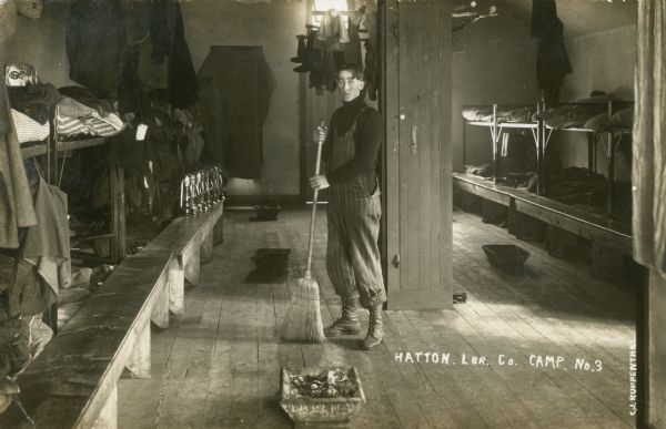 A man is sweeping the bunk house at Hatton Lumber Company Camp. Caption reads: "Hatton Lbr. Co. Camp No 3."