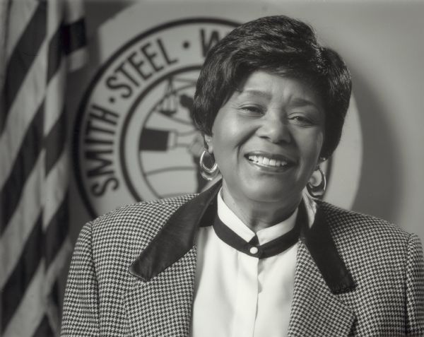 Portrait of Nellie Wilson posing in front of an American flag and a Smith Steel Workers logo.