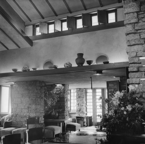 Living/dining room at Taliesin looking towards the Bird Walk. Much of the furniture in the image is Wright designed. There are various types of pottery displayed on a ledge below the clerestory windows. Taliesin was the summer home of architect Frank Lloyd Wright. Taliesin is located in the vicinity of Spring Green, Wisconsin.