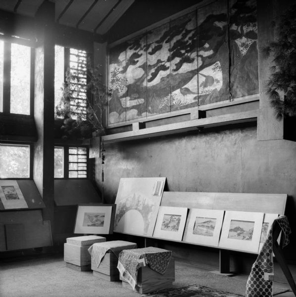 Art work, including Japanese prints, at Taliesin, the summer home of architect Frank Lloyd Wright. A large painted screen hangs on the wall, and fabric samples (possibly designed by Wright), with tags attached are draped over stools and easels. The Japanese prints displayed include Ukiyoe: The Pictures of the Floating World. Taliesin is located in the vicinity of Spring Green, Wisconsin.