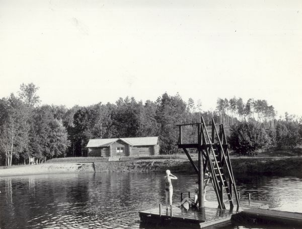 The bathing beach and bath house at Copper Falls State Park. Two swimmers are sitting and standing on a dock with a platform.