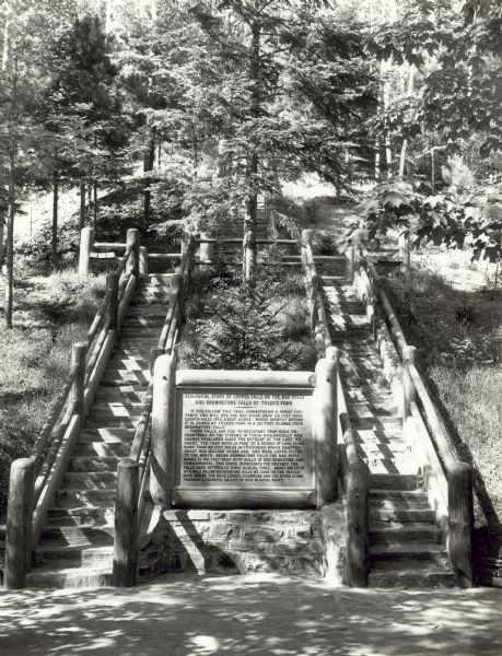 Two rustic stairways leading down to the Bad River at Copper Falls State Park. At the bottom of the stairs is a sign telling the geological story of Copper Falls and Brownstone Falls.