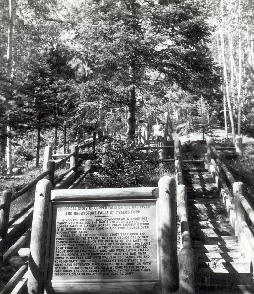 A sign giving the geological story of Copper Falls and Brownstone Falls at Copper Falls State Park. Barely visible in the background are two people at the top of the stairs.
