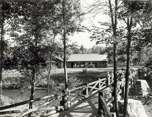 People on a rustic bridge over river at Copper Falls State Park. A long log building is in the background on the other side of the river.