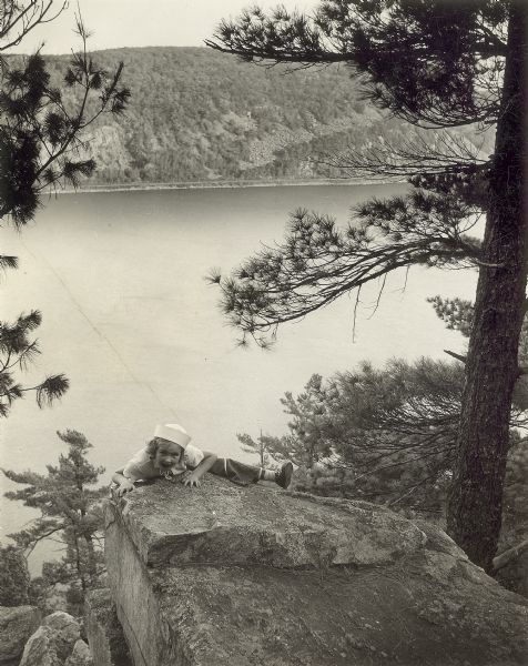 A girl climbing over the rocks at Devil's Lake State Park against a scenic view of the lake and surrounding areas.
