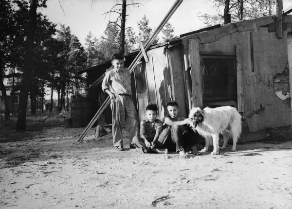 Three Indian children pose outside their home with a large, white dog.