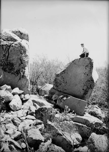 A young man sits atop a large boulder in a rock quarry.