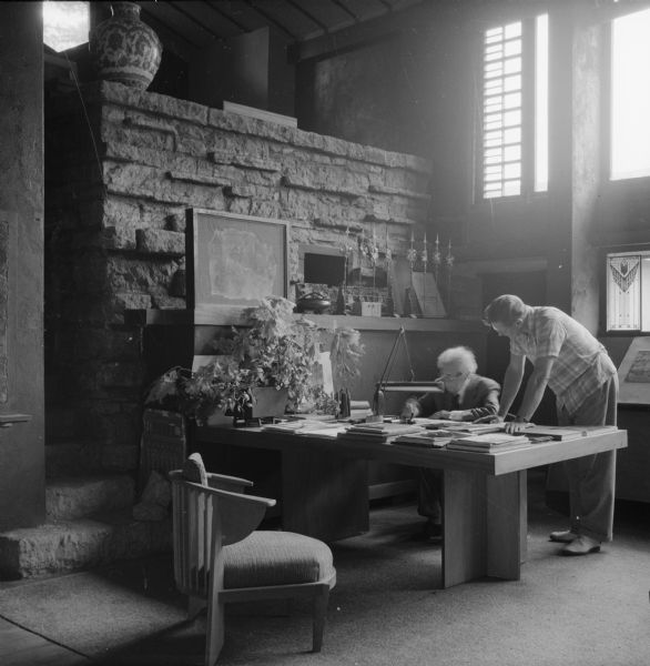 Architect Frank Lloyd Wright and an unidentified man are in Wright's studio at Taliesin, Wright's summer home, looking at drawings. Taliesin is located in the vicinity of Spring Green, Wisconsin.