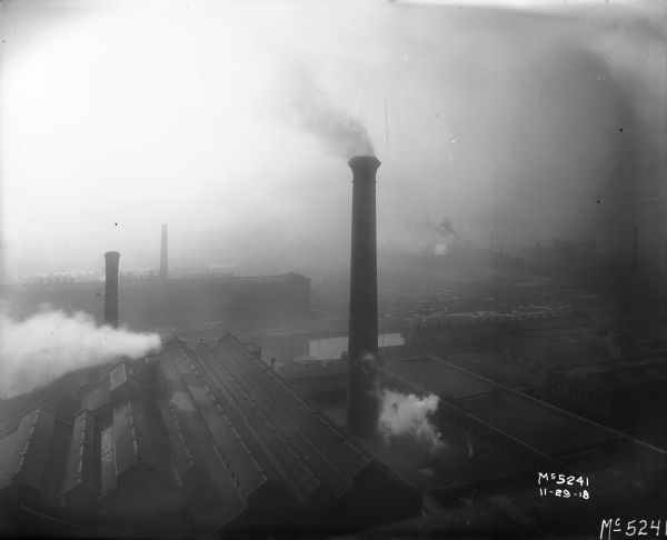 Elevated view of smokestacks on International Harvester's McCormick Works factory buildings. The sky is hazy and appears to be filled with smog or pollution.