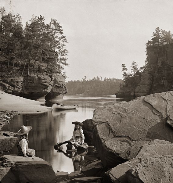 Jaws, from Stone Pile. Two children wearing straw hats are sitting on rocks in the foreground. A canoe is pulled up on a sandy bank in the background.