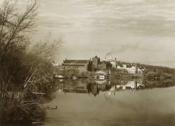 View along shoreline of University of Wisconsin-Madison buildings across Lake Mendota from Carroll Street. The Armory (Red Gym or Old Red), a boathouse, and Bascom Hall on Bascom Hill are in the background.