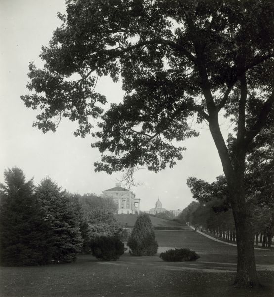 View of Agriculture Hall from a distance on the University of Wisconsin-Madison campus. Bascom Hall is in the background on Bascom Hill. The dome on Bascom Hall buned in October 1916, suggesting this photograph was taken prior to that date. The flag pole was added after 1908.