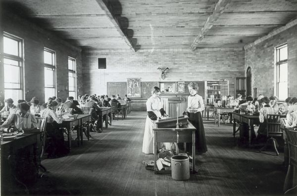 A class of male and female students work in a biology laboratory at the University of Wisconsin-Madison. Two women stand in the middle of the large, open room near a sink.