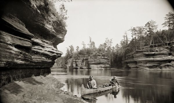 Two men near shoreline in a canoe opposite Steamboat Rock.