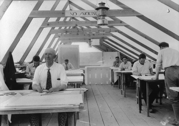 Drafting room used by the Taliesin Fellowship at Ocatilla. A number of Fellowship apprentices are working at drafting tables.