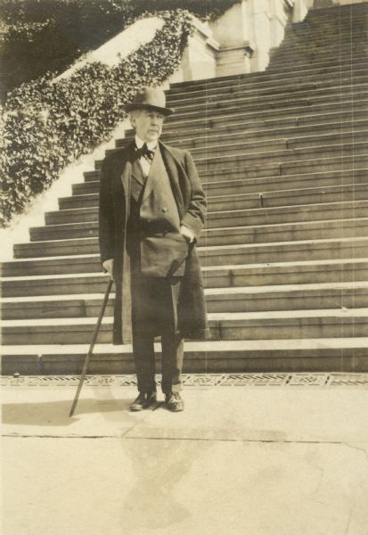 Full-length portrait of Frank Lloyd Wright standing at the foot of the steps of the national Capitol.