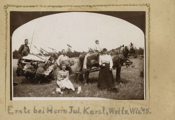 Women bringing lunch to the men working in the field. The men are harvesting grain using a horse-drawn grain binder.