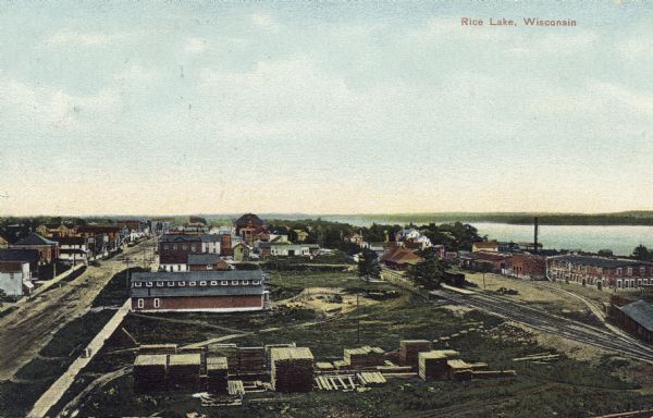 Elevated view of the city of Rice Lake with a lumber yard in the foreground, a railroad and Rice Lake at left. Caption reads: "Rice Lake, Wisconsin."