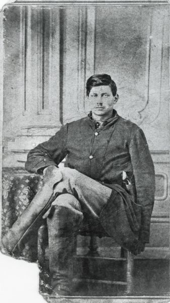 Seated portrait of George F. Pond wearing a long coat with a pistol in the pocket and knee-length boots.