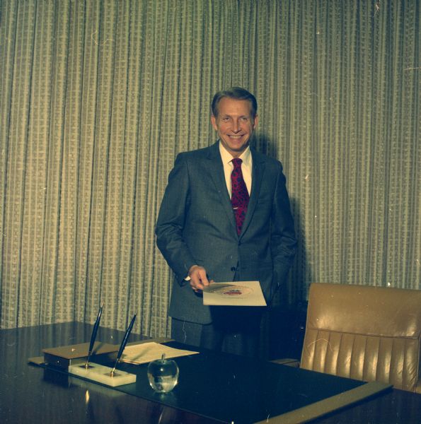 Portrait of J.M. Smucker Company executive Paul Smucker standing next to his desk holding a brochure.