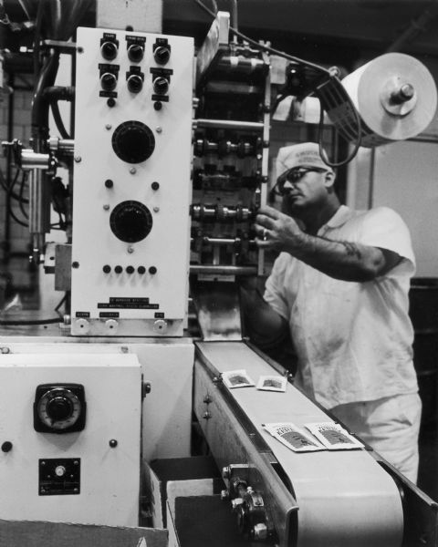 A man is operating the portion control/ketchup packet machine at a J.M. Smucker Company plant.