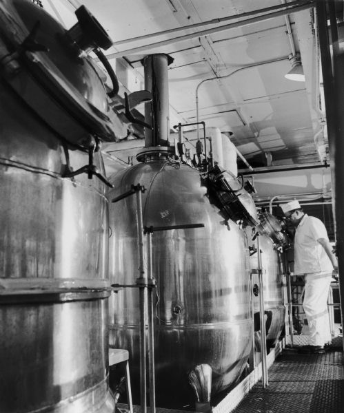 A man is examining a giant vacuum kettle at a J.M. Smucker Company Plant. Original caption read:, "Giant vacuum kettles are used to cook Smucker's preserves, insuring a perfect blend of the pure fruit with sugar, while the fruit essence cooked off here is cooled and added back into the finished product before being put into jars."