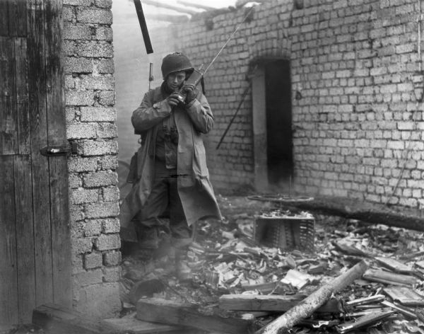 PFC Harold C. Schreckengost, commanding officer's runner, using a walkie-talkie among the rubble of buildings, directs movements of Company E, 2nd Battalion, 2nd Division, 1st U.S. Army.