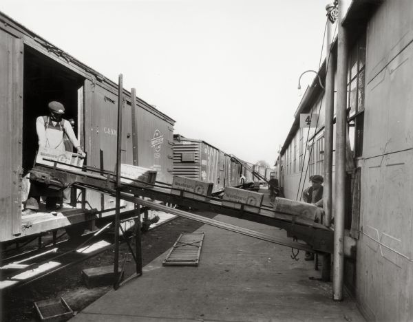 Two men loading boxes of batteries onto railroad cars with a conveyor belt. French Battery later became Ray-O-Vac Corporation.
