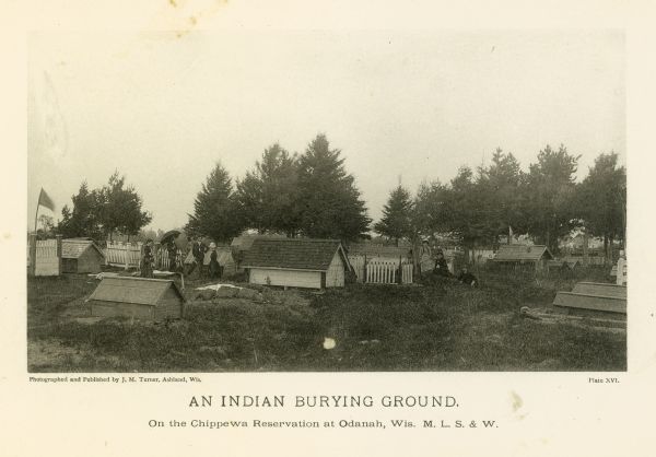 View of an Indian cemetery on a Chippewa reservation. People are posing among the graves.