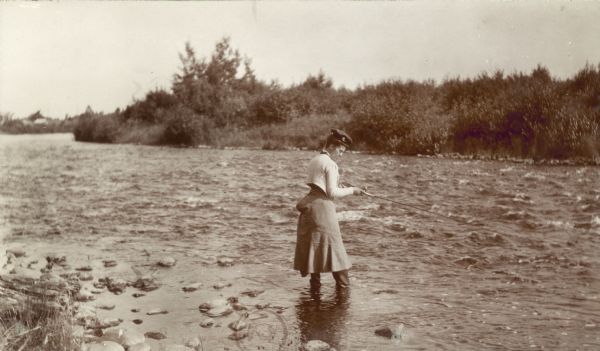 A fashionably dressed woman fishes for trout while standing in the Namekagon River.
