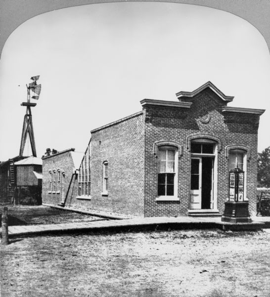 Exterior of the front and east side of the Bennett Studio when it was new, showing the skylight and the revolving print house. There is a large windmill behind the building.