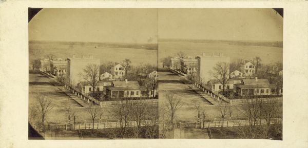 South Pinckney Street as photographed by Fuller from the Wisconsin State Capitol roof. In the center are several wooden structures dating from Madison's earlier years. The State Bank, seen on the left, is typical of the more permanent stone buildings that were beginning to replace them. The Williamson and Marquette neighborhoods are in the background and Governor Farwell's Octagon House is in the center on the shore of Lake Monona.