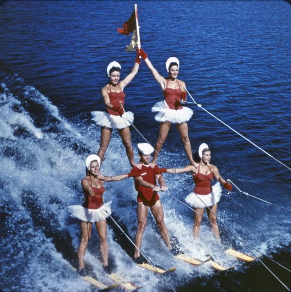 Elevated view of pyramid of water skiers in Tommy Bartlett's show on Lake Delton. The woman on top of the pyramid holds a red flag.