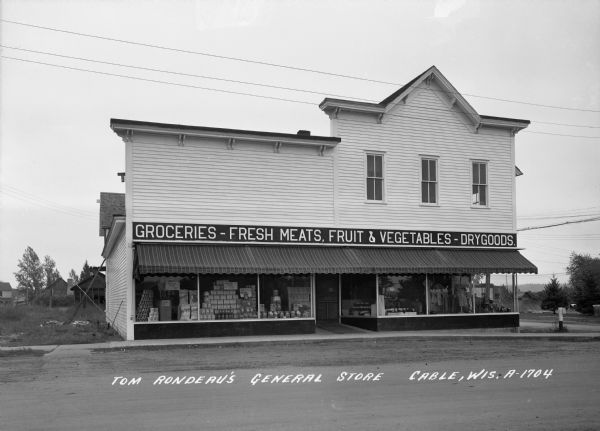 Exterior view from street of the storefront. Caption reads: "Tom Rondeau's General Store, Cable, Wis."