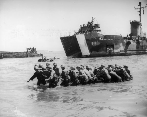 A cordon of GI's work together in water to move a submerged jeep to the beach of Leyte Island.