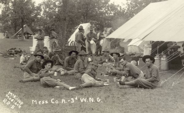Soldiers have a meal while sitting on the grass outside the mess tent, possibly at Camp Douglas.