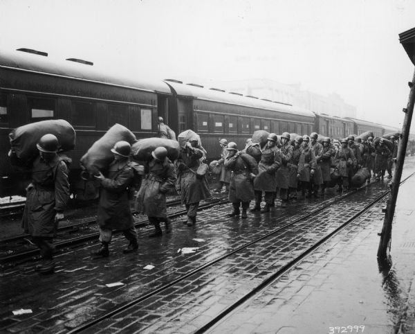Personnel of the 24th US Infantry Division, carrying duffel bags, prepare to board a train to Northern Japan.