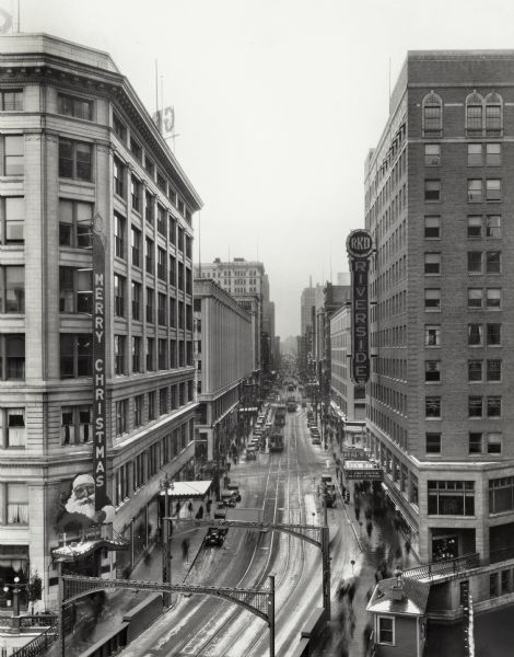 Elevated view down Wisconsin Avenue looking west, with the RKO Riverside Theatre on the right, and a large Christmas sign on the corner of a building on the left.