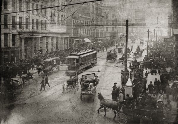 Elevated view of busy street scene in downtown Milwaukee at the turn of the century showing a trolley, horse-drawn vehicles and pedestrians near an intersection.