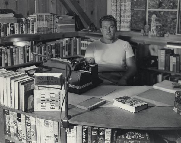Author August Derleth surrounded by books at his desk.