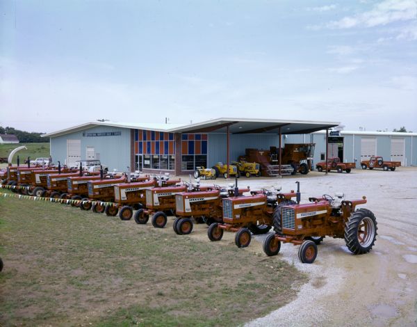 Color photograph of Farmall tractors, International utility tractors, and combines lined up outside Otter Sales and Service, an International Harvester dealership.